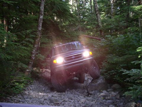 1979 Ford Bronco - Ford Bronco tackling a challenging rocky path through a dense forest, likely a 1992-1996 model.