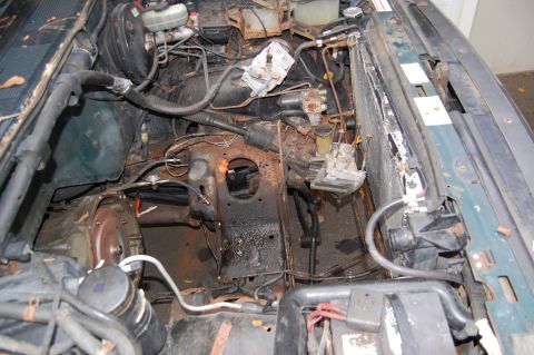 1994 Ford Bronco - The engine bay of a dark green vehicle shows extensive rust and corrosion on various components.