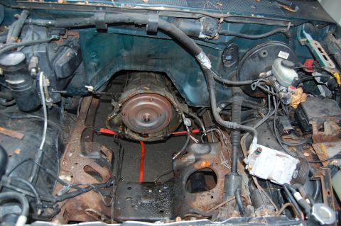 1994 Ford Bronco - The engine bay of a vehicle, with the transmission removed, revealing a rusty frame and brake booster assembly.