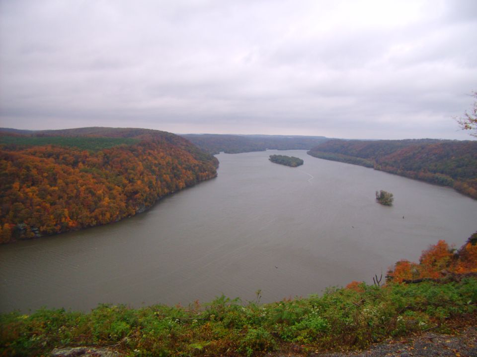 River winding through hills covered in orange and green autumn trees under a cloudy sky