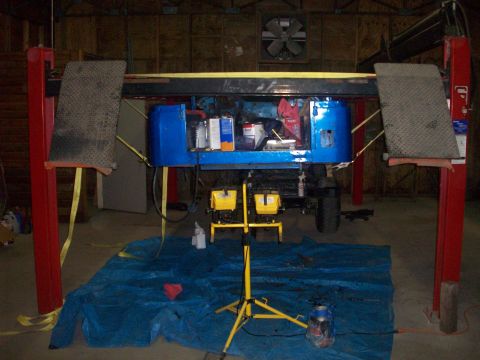 1978 Jeep CJ5 - A blue Jeep body is suspended on a car lift, revealing its interior and various containers.