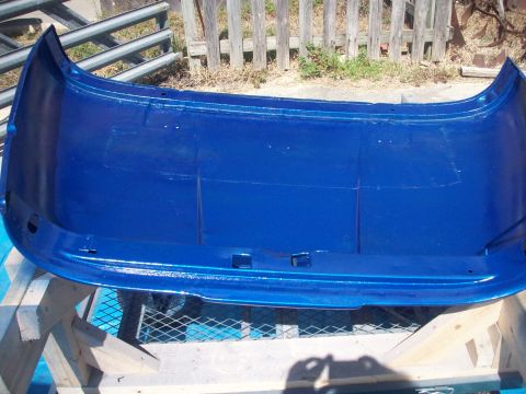 1978 Jeep CJ5 - A blue painted car bumper is shown from its interior side, supported by wooden beams against a wooden fence backdrop.