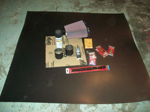 1985 Ford Bronco - Various automotive parts and supplies, including an air filter and spray paint, are arranged on a dark mat.