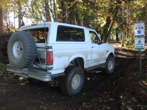 1978 Ford Bronco - A white Ford Bronco is parked on a muddy trail surrounded by trees with autumn leaves.