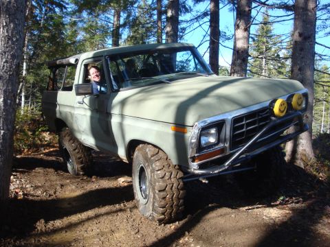 1978 Ford Bronco - A 1978 Ford Bronco navigates a muddy, wooded trail with a driver smiling from the window and custom smiley face headlights.