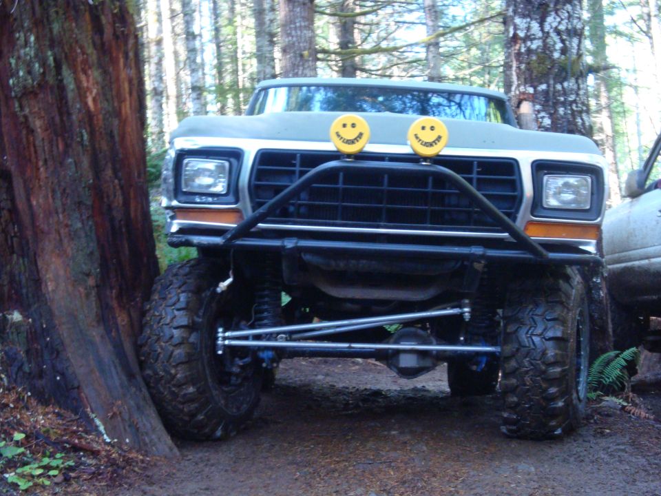1978 Ford Bronco with custom bumper and smiley face lights, parked in a forest
