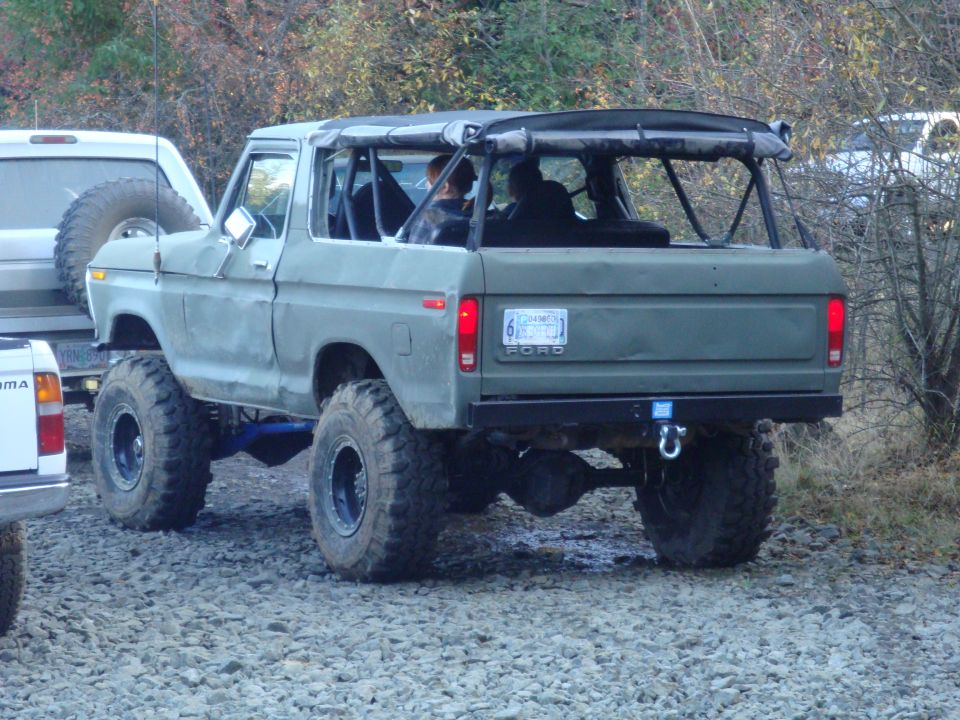 Rear view of a lifted 1978 Ford Bronco with a soft top and off-road tires. Another SUV and a pickup truck are partially visible