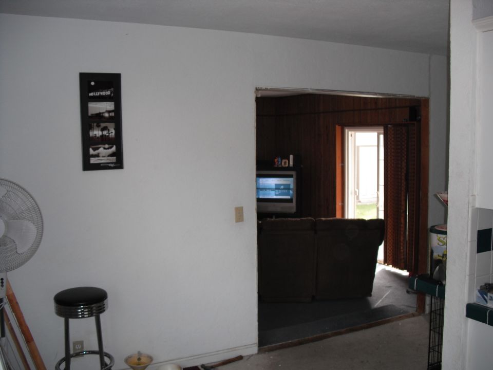 Interior view of a room with a fan, stool, and doorway to another room with a TV and couch