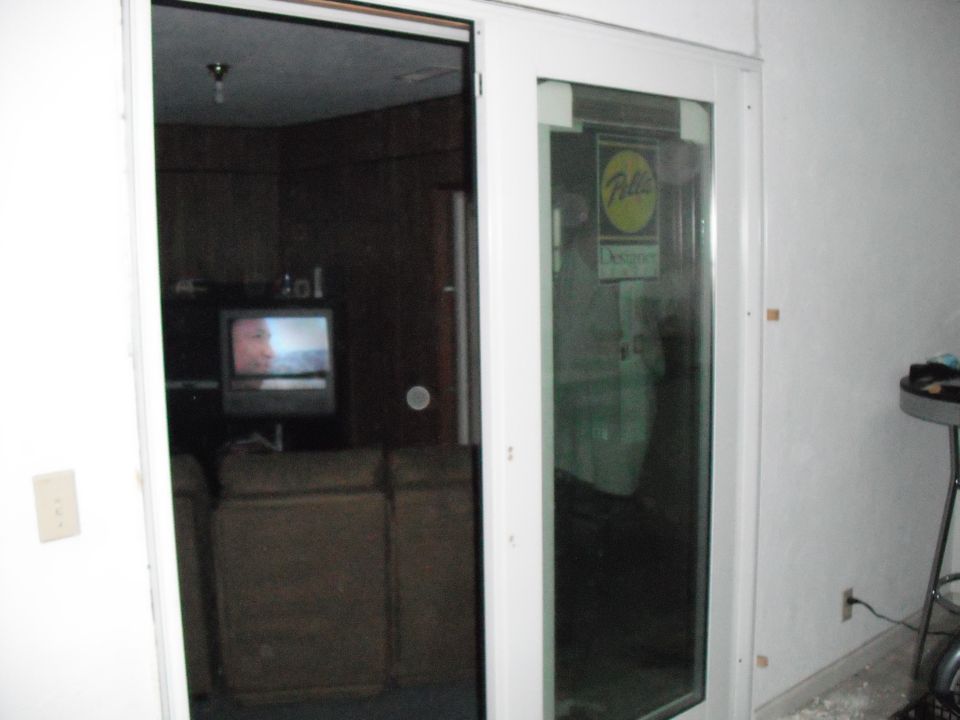 Interior room with TV and couch visible through a glass door. A yellow and green sign is on the glass