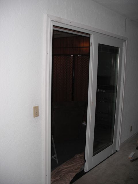 1991 Ford Bronco - A sliding glass door with a screen is shown, leading into a dimly lit room with wood paneling and a patterned curtain.
