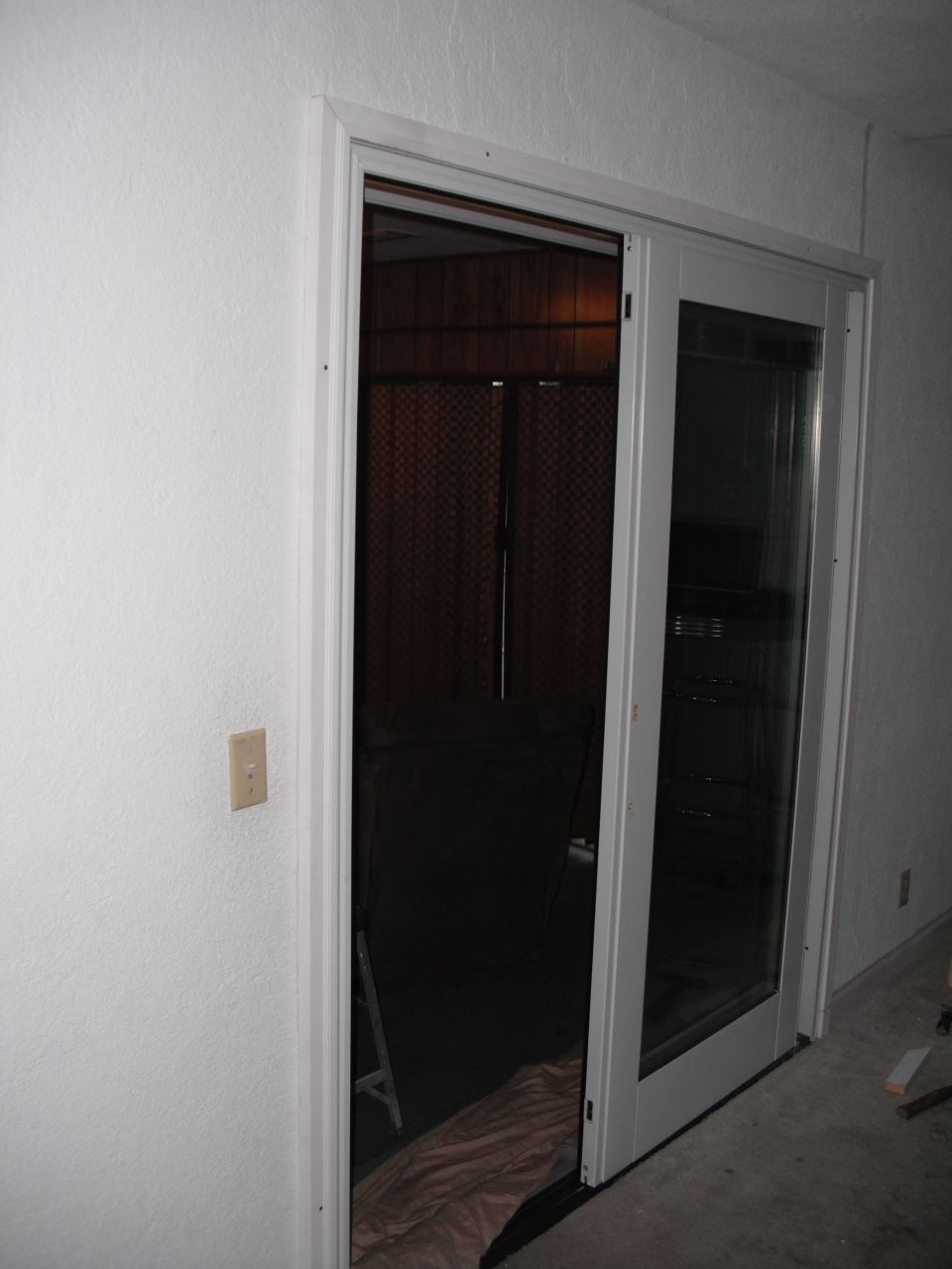 Sliding glass door with a screen, leading to a dark room with wood paneling