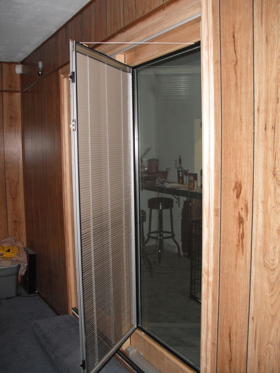 Open screen door with blinds, revealing a bar area with stools and bottles