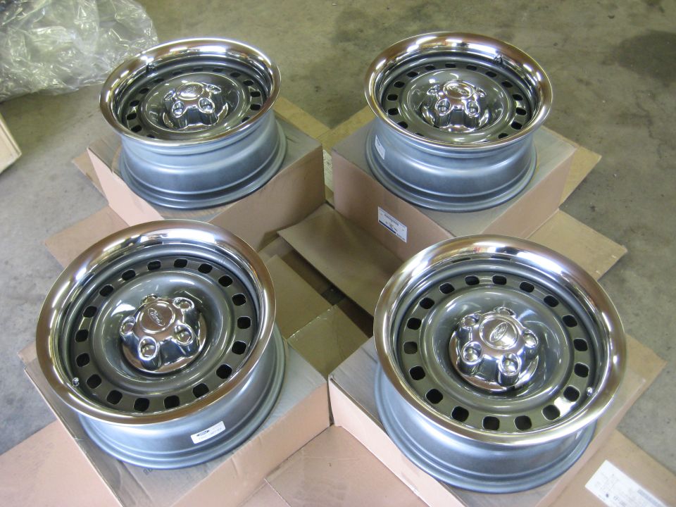 Four gray Ford steel wheels with chrome trim rings and center caps sitting on cardboard boxes