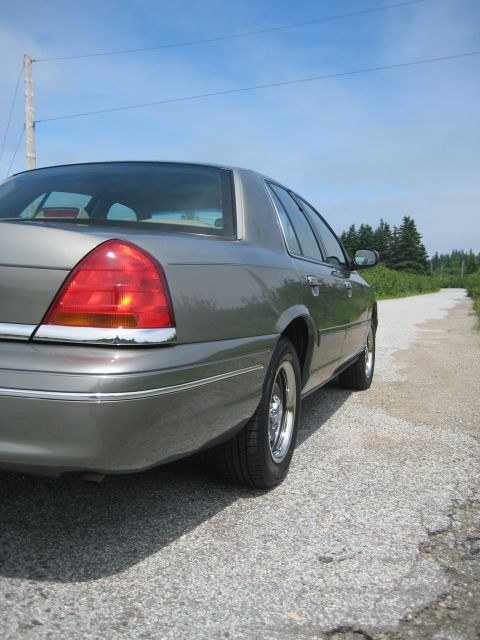1999 Ford Crown Victoria - Grey sedan parked on a gravel road under a clear blue sky.