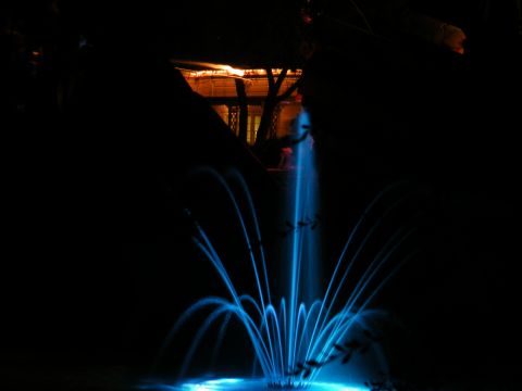 1982 Ford Bronco - A fountain sprays water illuminated by blue lights against a dark background, with a building visible in the distance.