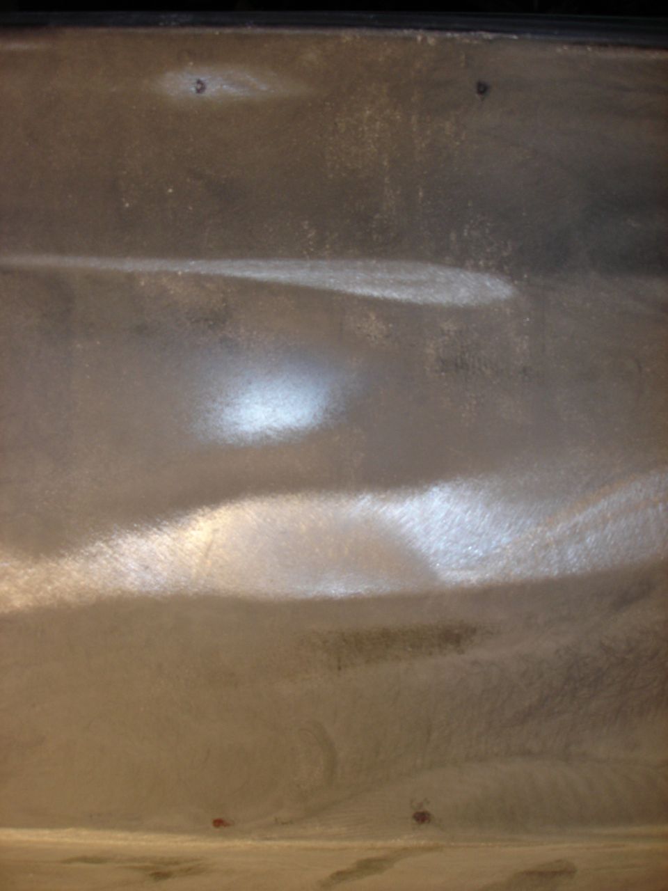 Truck bed with visible dents and scratches, showing a metallic sheen under light