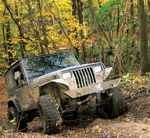 1991 Jeep Wrangler - A muddy 1991 Jeep Wrangler navigates a wooded trail during autumn.