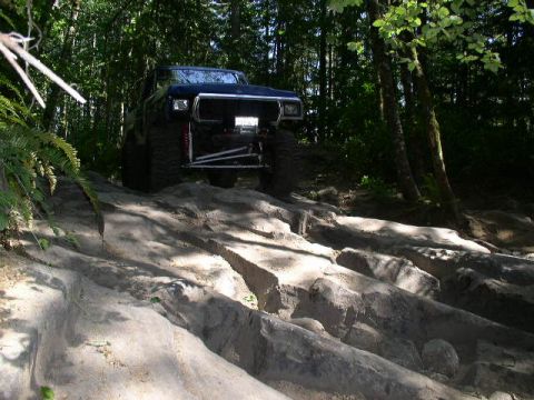 1979 Ford Bronco - A dark blue 1978 Ford Bronco navigates a challenging rocky terrain in a wooded area.