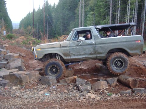 1978 Ford Bronco - A modified 1978 Ford Bronco is shown navigating a challenging off-road course with large rocks and logs.