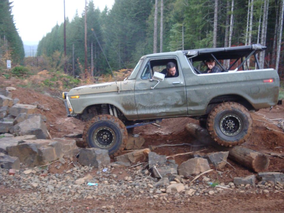 Green 1978 Ford Bronco off-roading over rocks and logs