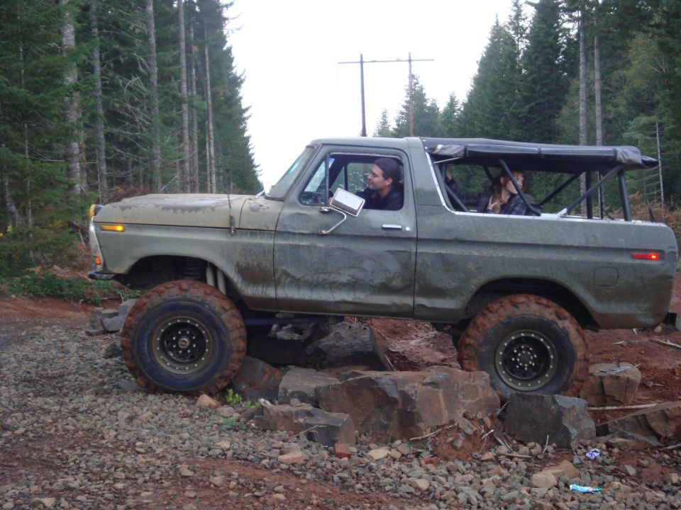 Olive green 1978 Ford Bronco with a soft top, driving over rocks on a dirt road