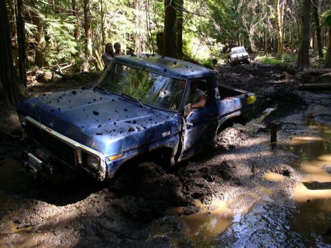 1979 Ford Bronco - A blue 1979 Ford Bronco is stuck deep in the mud while another vehicle is visible in the background.