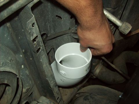 1985 Ford Bronco - Hand installs a PVC pipe fitting in the engine bay, obscuring vehicle details.