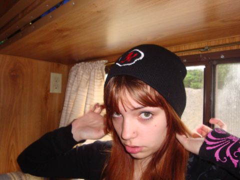 1978 Ford Bronco - A young woman with red hair wears a black beanie with a red and white logo while inside a wood-paneled room.
