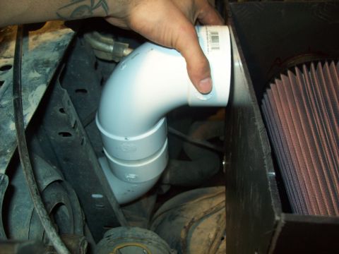 1985 Ford Bronco - A hand installs a custom PVC intake pipe connected to a K&N air filter in the engine bay of a vehicle.