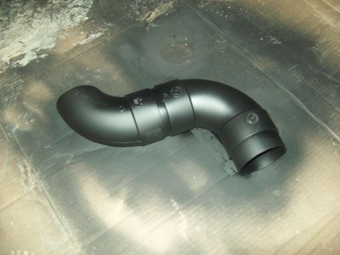 1985 Ford Bronco - A black, curved air intake hose with visible clamps is shown against a textured background.