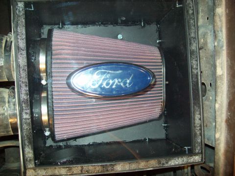 1985 Ford Bronco - Close-up of a Ford oval logo affixed to a conical air filter within its housing.