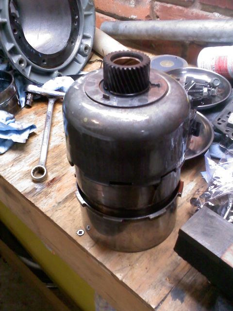 1977 Ford F-100 - A disassembled torque converter part sits on a wooden workbench next to tools and other automotive components.