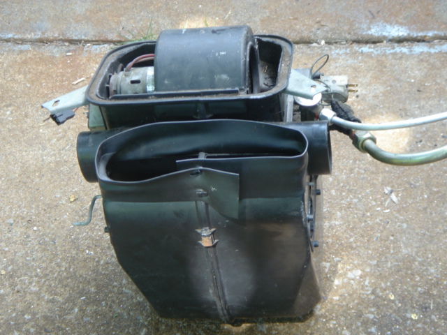 Removed heater box and blower motor assembly on concrete, with wiring and hoses attached