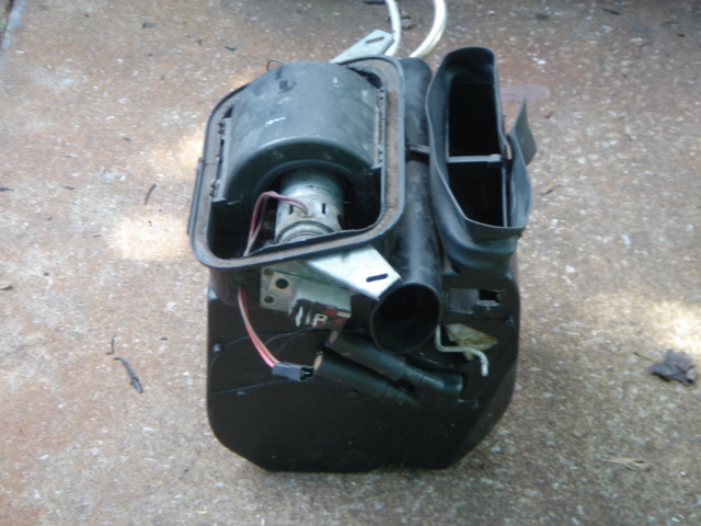Disassembled black heater box with blower motor and ductwork on concrete
