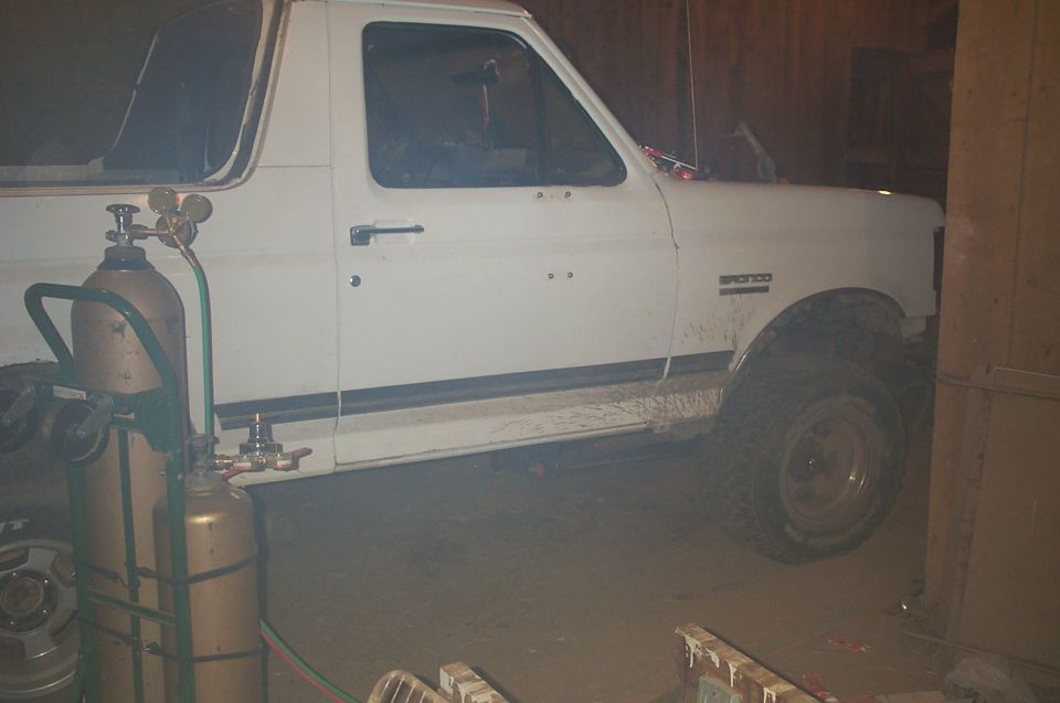 White Ford Bronco parked in a dark garage with a welding torch tank cart in the foreground