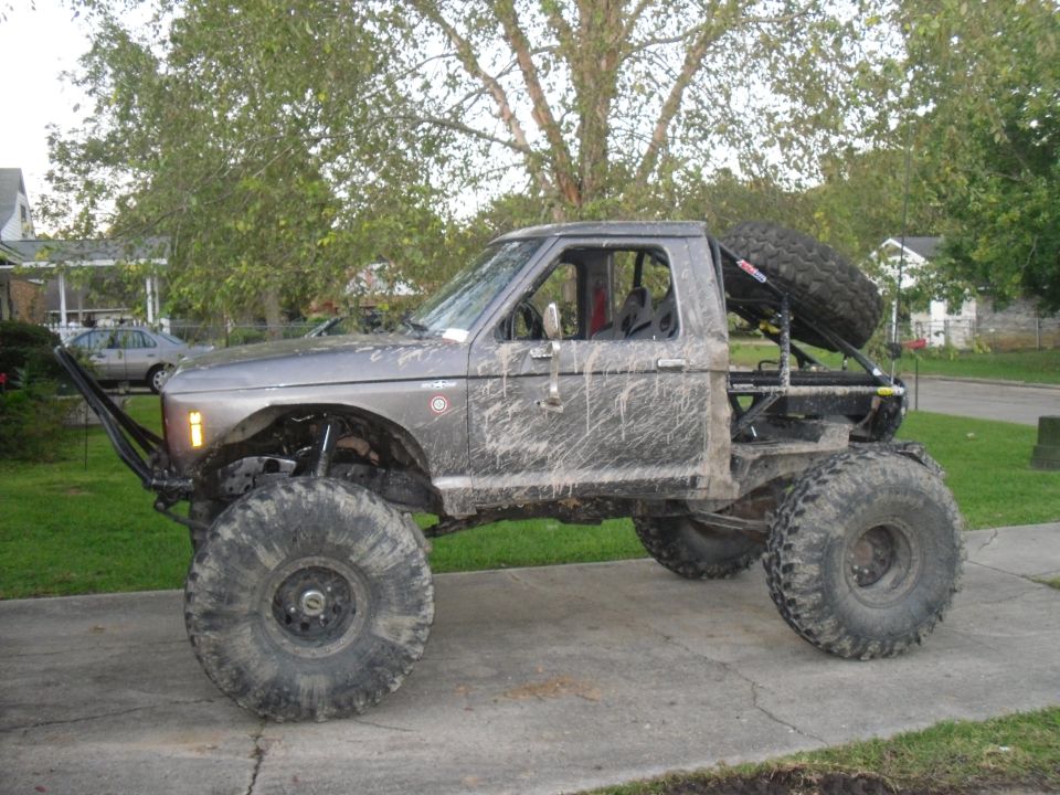 Mud-splattered gray Ford pickup truck with oversized tires and a roll cage, viewed from the side