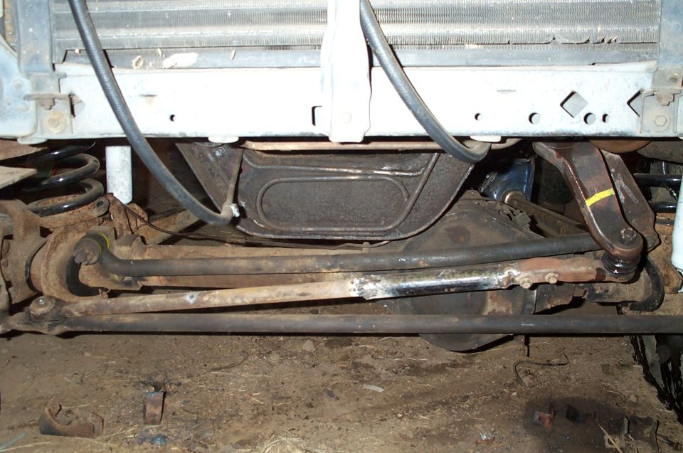 Under-front view of a Bronco's front axle, tie rod and drag link steering linkage, coil spring, and radiator bottom