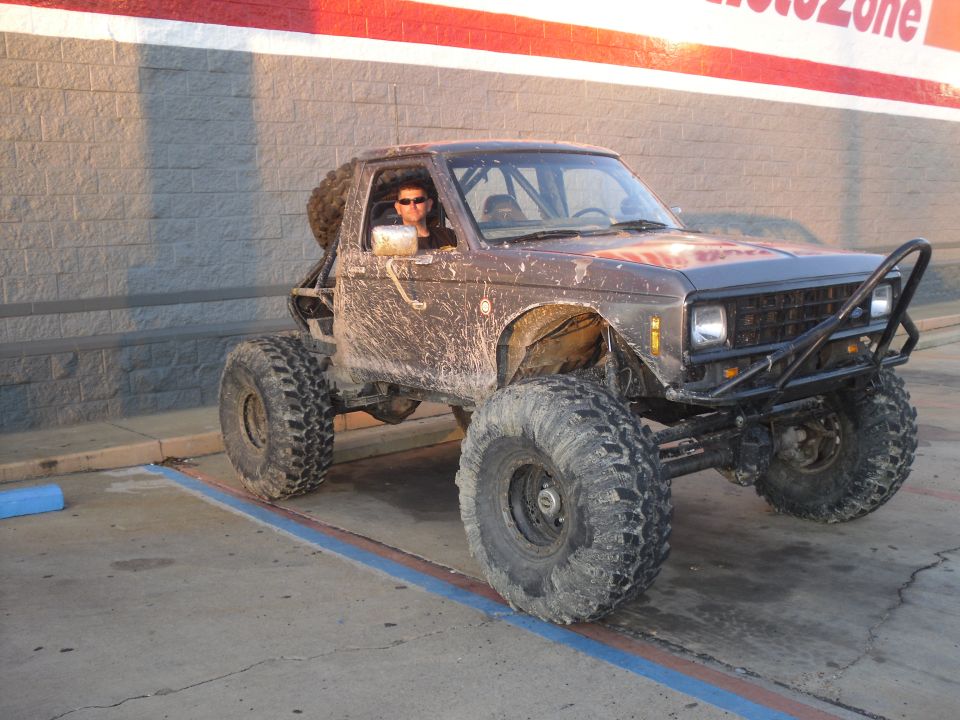 Lifted, doorless brown Bronco II off-road rig on big muddy tires parked outside AutoZone
