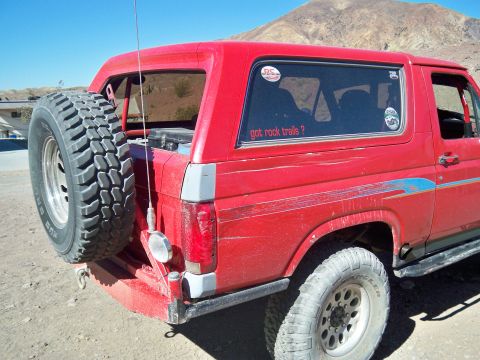 1985 Ford Bronco - This red Ford Bronco is equipped for off-road adventures, a rear-mounted spare tire and a sticker asking about rock trails.