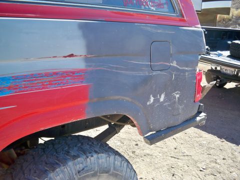 1985 Ford Bronco - Rear view of a damaged SUV, showing its quarter panel and fuel door. A second vehicle is in the background.