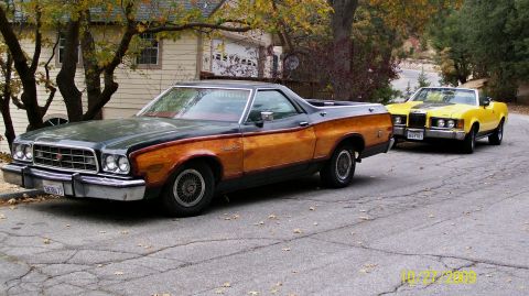 1973 Ford Ranchero - A dark green and wood-paneled Ford Ranchero is parked on a residential street, with a yellow convertible behind it.