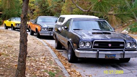 1973 Ford Ranchero - A line of Rancheros, including a dark blue 1973 model with a camper shell, parked on a roadside.