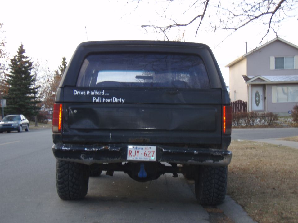 Rear view of a black 1985 Ford Bronco with a sticker that says "Drive it in Hard... Pull it out Dirty"