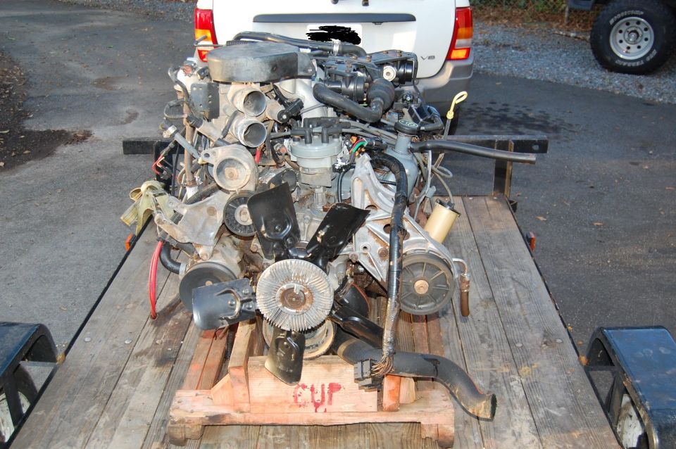 Engine on a wooden trailer, front view. Some hoses and belts are visible