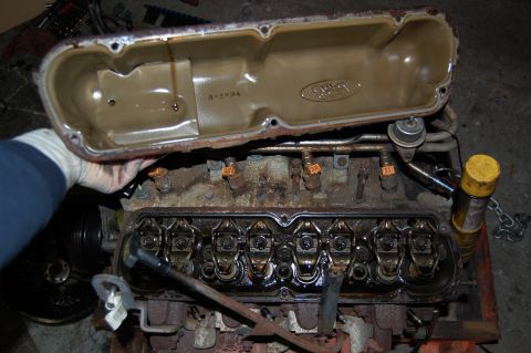 1994 Ford Bronco - A valve cover with a "3-2-94" date stamp and Ford logo is held over an engine.