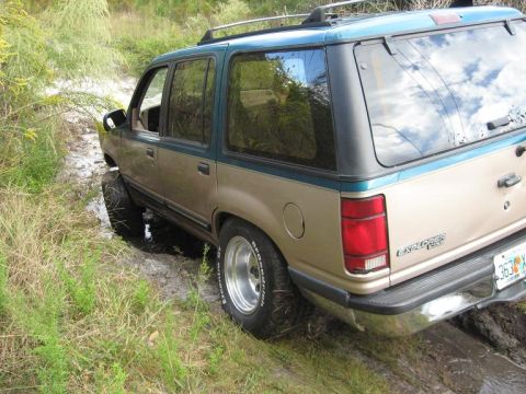 1992 Ford Explorer - This two-tone Ford Explorer is navigating a muddy trail with its tires partially submerged.