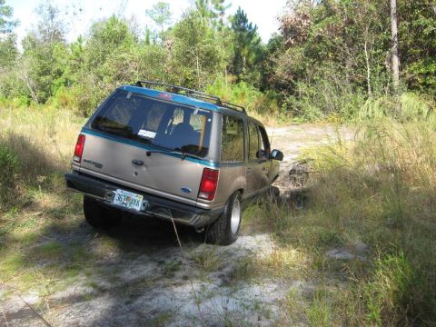 1992 Ford Explorer - A 1992 Ford Explorer navigates a dirt path surrounded by tall grass and trees.
