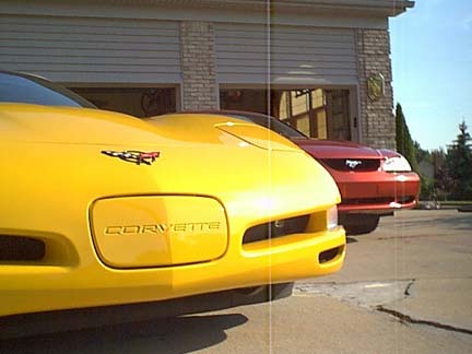 1994 Ford Mustang - A yellow Corvette is parked in front of a red Mustang, with both vehicles in front of a garage.
