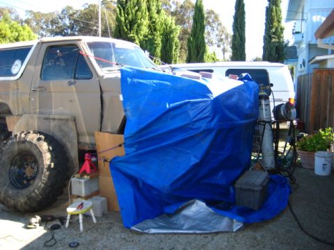 1989 Ford Bronco - A modified Ford Bronco sits in a driveway, partially covered, with a van and welding equipment nearby.