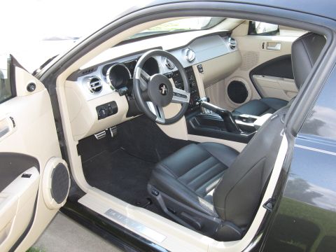 1996 Ford Bronco - The interior of a car is shown, black leather seats, a tan dashboard, and a prominent Mustang emblem on the steering wheel.